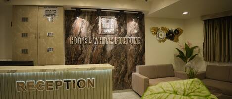 A hotel reception area with a marble wall, a clock, and a reception desk labeled "RECEPTION".