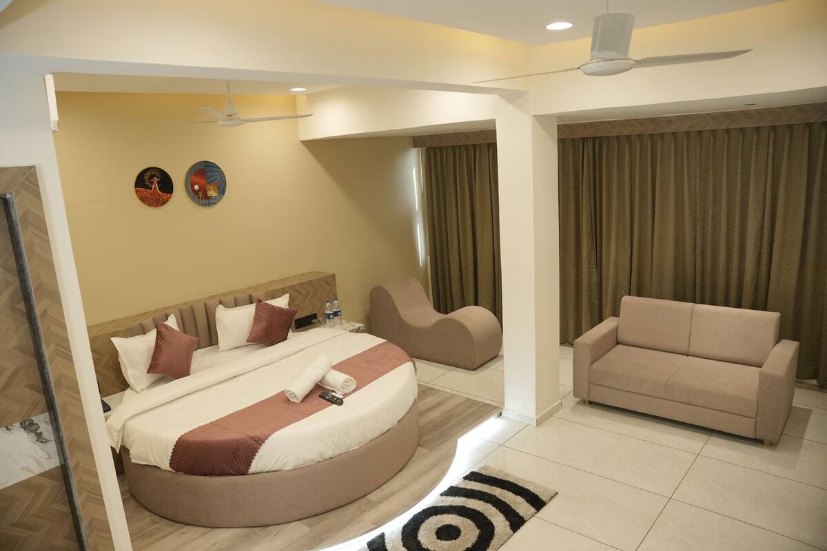 Quarto de hotel moderno com uma cama redonda, um sofá, um ventilador de teto e duas obras de arte na parede.