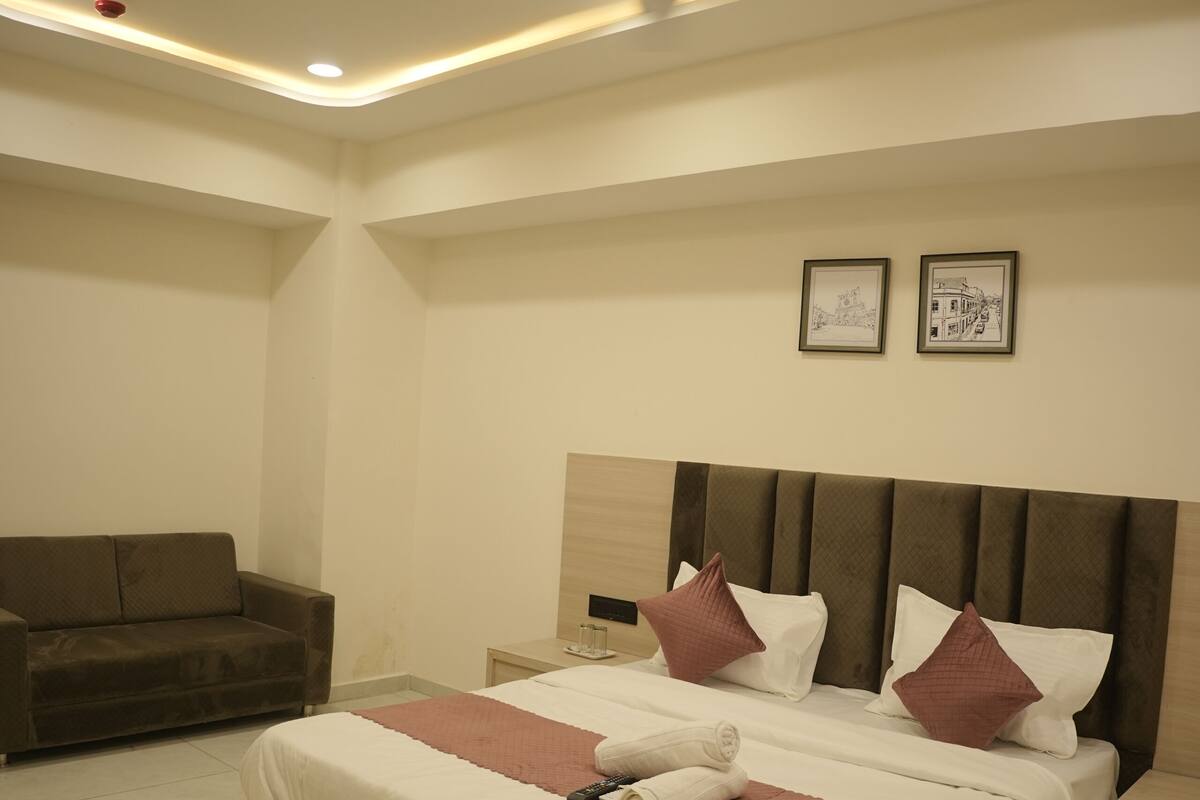 Quarto moderno com cama grande, mesa de cabeceira, sofá e iluminação embutida no teto.
