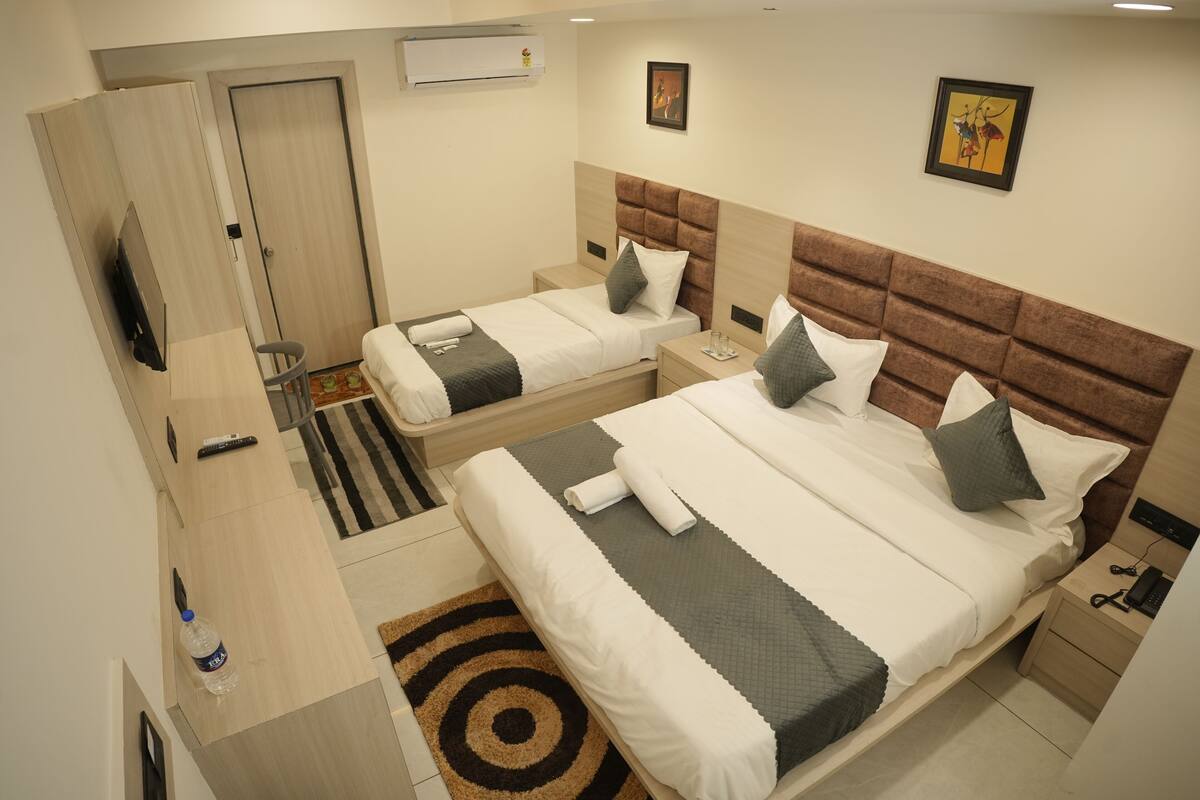 Quarto de hotel com duas camas, televisão, guarda-roupa e banheiro.