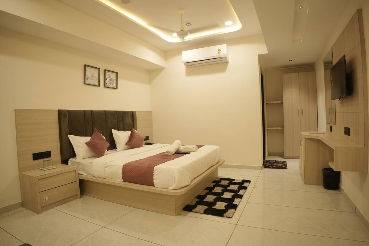 Um quarto moderno com cama, mesas de cabeceira, iluminação no teto, aparelho de ar condicionado, televisão e guarda-roupa.