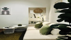 A modern living room with a white sofa, two round side tables, and a decorative shelf with plants and a lamp.