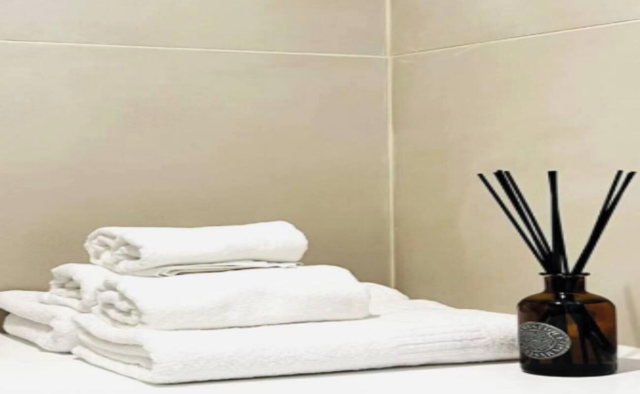 A stack of white towels and a reed diffuser in a corner of a room with plain walls.