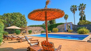 Un espace piscine avec des chaises longues et un parasol en chaume.