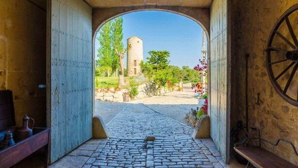 Un portail en arc donnant sur un chemin pavé de pierres, avec vue sur une tour et sur la verdure.