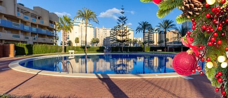 A swimming pool with a brick walkway, palm trees, and a building complex in the background.
