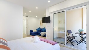 A modern hotel room with a bed, a sofa, a TV, and a sliding glass door leading to an outdoor seating area. - Amazing Between Two Seas by Fidalsa (Murcia)