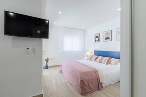 A modern hotel room with a flat-screen TV mounted on the wall, a bed with a blue headboard, and a window with white curtains. - Amazing Between Two Seas by Fidalsa (Murcia)