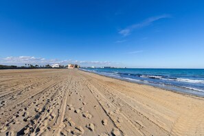 A wide sandy beach with footprints leading to the water, a clear blue sky, and buildings in the distance. - Amazing Between Two Seas by Fidalsa (Murcia)