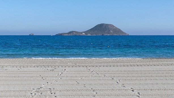 A beach with footprints leading to the water, a sailboat, and a distant hill. - Amazing Between Two Seas by Fidalsa (Murcia)