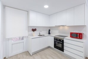 A compact kitchen with white cabinetry, a black oven, a red microwave, and a small sink. - Amazing Between Two Seas by Fidalsa (Murcia)