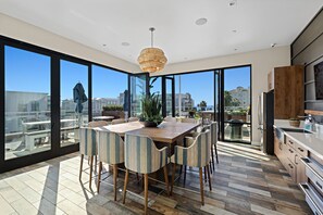A modern kitchen with a large island, a dining area with striped chairs, and large windows offering a view of the city.