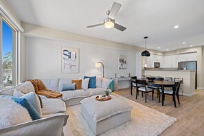 Ein modernes Wohnzimmer mit einer Couch, einem Hocker und einem Essbereich mit Stühlen und einem Tisch.