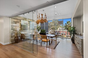 Un intérieur moderne avec une cloison en verre, un plancher en bois, un coin repas avec des chaises et une table, et un panneau indiquant un centre d’affaires.