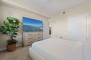 Ein Schlafzimmer mit einem Bett, einem Schminktisch, einem Fernseher und einer Zimmerpflanze.