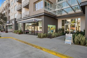 Un bâtiment moderne avec une entrée en verre, des places assises à l’extérieur et une enseigne indiquant une vente.