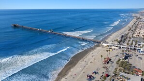 Une jetée qui s’avance dans l’océan, avec une plage et des bâtiments à proximité.