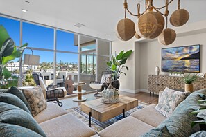A spacious living room with a large window, a modern sofa set, a coffee table, and a hanging light fixture.