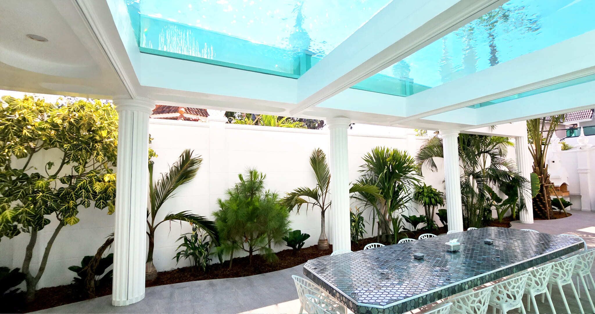 A modern outdoor patio with a glass ceiling, white columns, and a mosaic-topped table surrounded by white chairs.