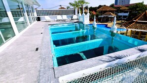 A rooftop pool with clear blue water, surrounded by white chairs and a white fence.