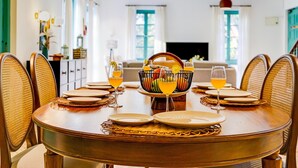 A dining area with a round table set for four, surrounded by wicker chairs. A fruit bowl and glasses of orange juice are on the table. - Villa in Siolim Near Morjim Beach (Siolim)