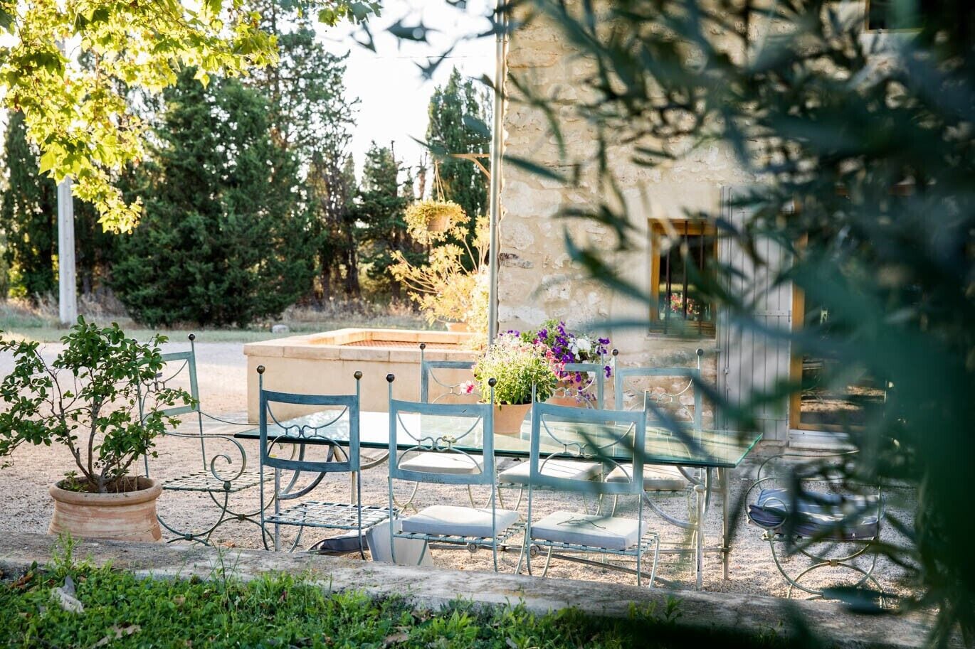 A rustic outdoor seating area with metal chairs and a table, surrounded by potted plants and a stone wall.