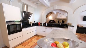 A modern kitchen with white cabinetry, a built-in oven, and a central island with a stainless steel bowl containing fruits.