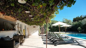 A poolside area with lounge chairs, a wooden bench, and a pergola covered with vines.