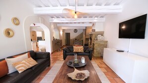 A living room with a dark brown coffee table, two black sofas with orange cushions, a white entertainment unit, and a flat-screen TV.