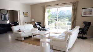 A spacious living room with a white sofa, a coffee table, and a black leather chair. A large window offers a view of mountains. - Holiday rental villa view and pool AUREILLE LS1-449 (Aureille)