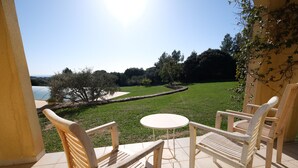A patio with two wooden chairs and a small round table, overlooking a grassy area with trees and a body of water. - Holiday rental villa view and pool AUREILLE LS1-449 (Aureille)