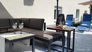 Een terras met een bank, een tafel en twee blauwe fauteuils.