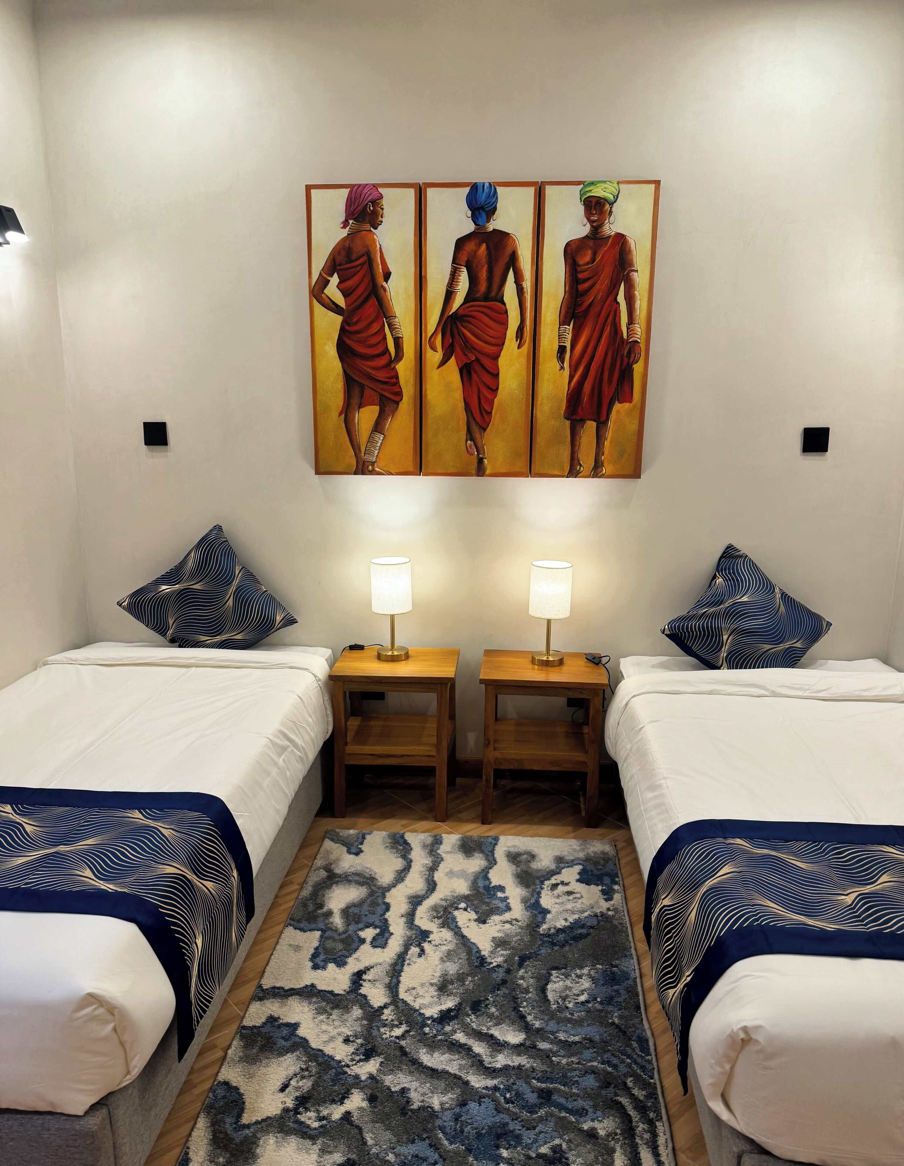 Habitación de hotel con dos camas, un tapete estampado y un cuadro con la imagen de tres personas.