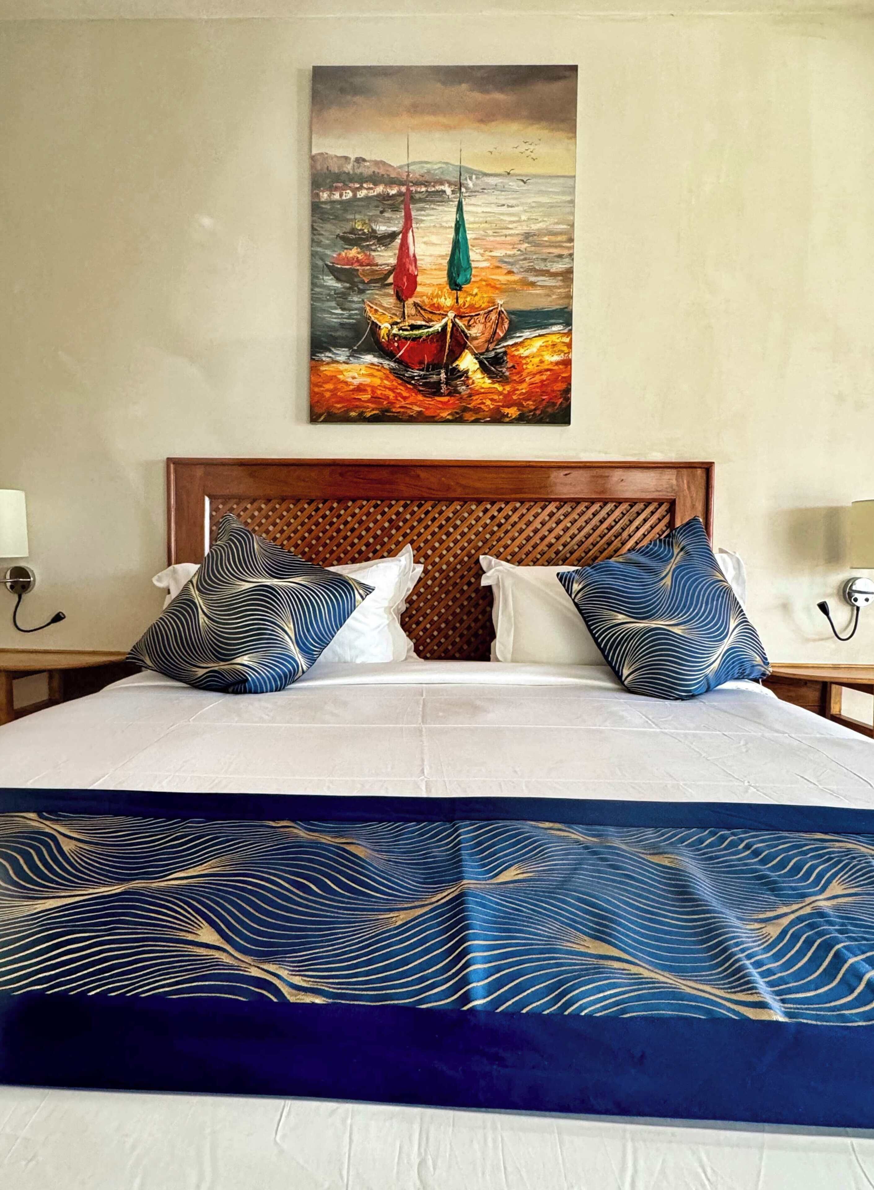 A hotel room with a bed, a painting of sailboats, and a wooden headboard.
