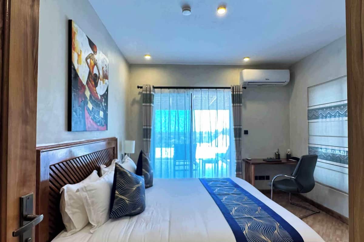 A modern hotel room with a large bed, a desk, and a view of the outdoors.