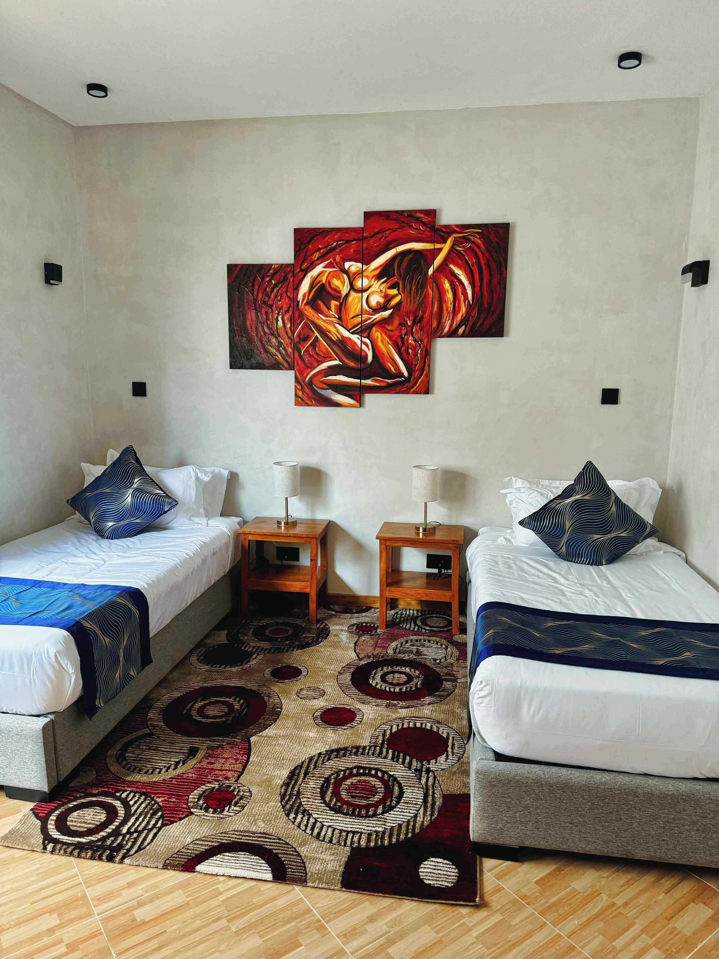 A hotel room with two single beds, a large abstract painting on the wall, and a patterned rug on the floor.