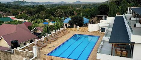 A swimming pool with lounge chairs and umbrellas, surrounded by buildings with varied roof colors.