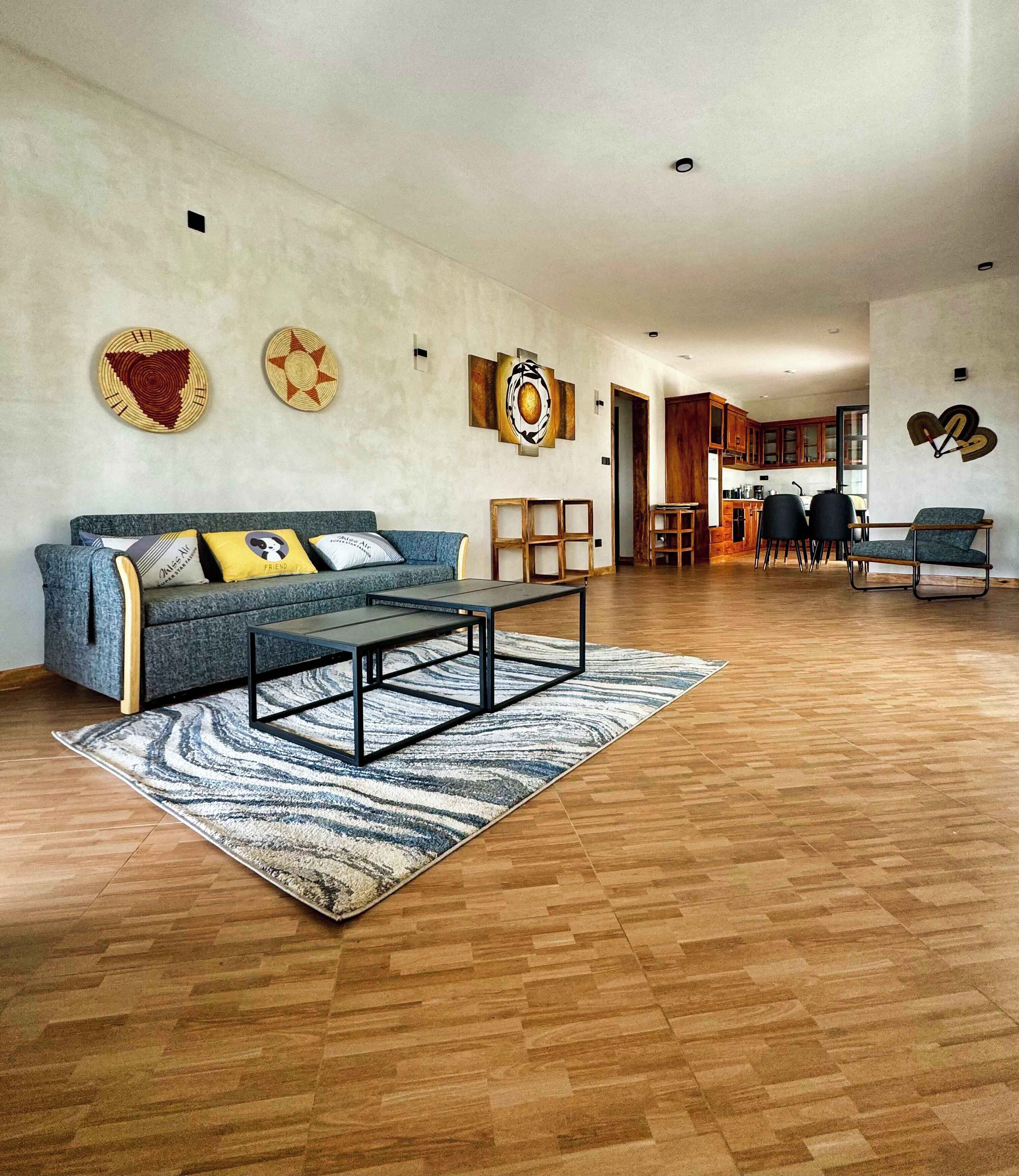 Amplia sala de estar con sofá, mesa de centro y alfombra. Se observan armarios de madera y un comedor al fondo.