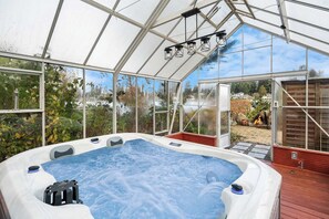 Un bain à remous installé à l’intérieur d’une serre, avec vue sur l’extérieur.
