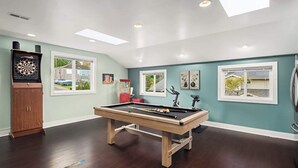 A pool table in a room with teal walls, a dartboard, and a jukebox.