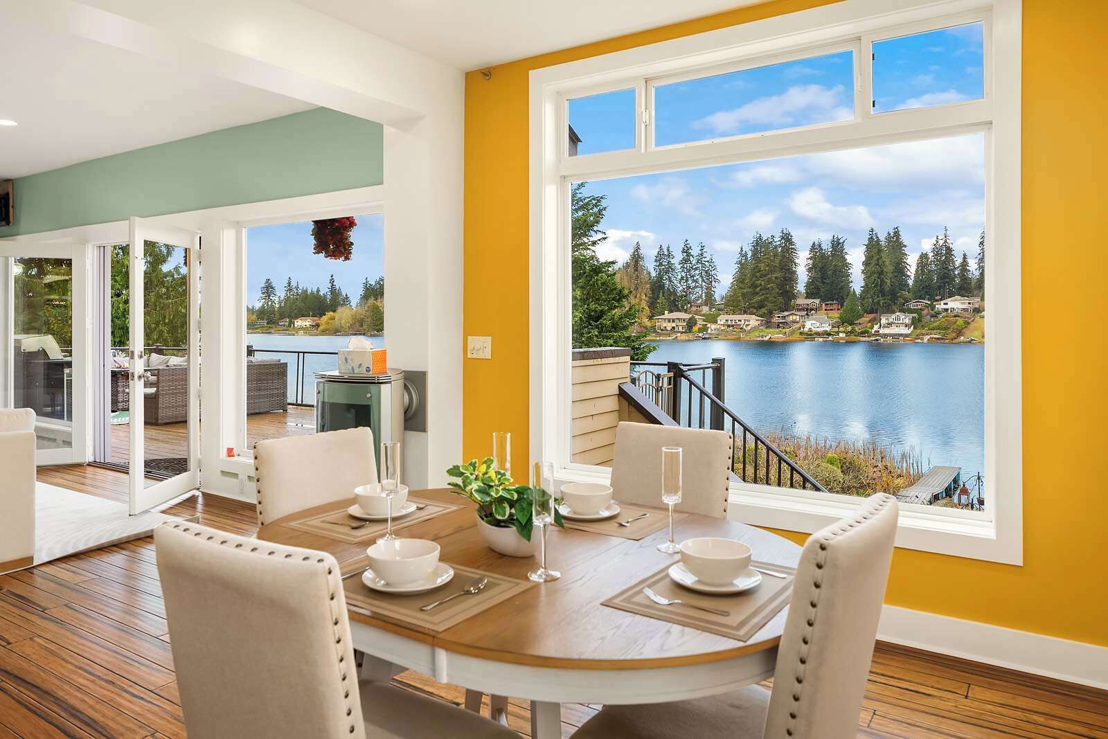 Un coin repas avec une table dressée pour deux personnes, une vue sur un lac et un balcon agrémenté de mobilier d’extérieur.