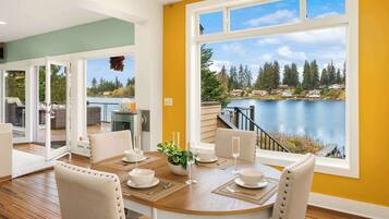 Un coin repas avec une table dressée pour deux personnes, une vue sur un lac et un balcon agrémenté de mobilier d’extérieur.