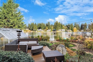 A patio with wicker furniture, a greenhouse, and a lake view. - Serene Waterfront Escape w, Amazing View & Hot Tub (Lynnwood)