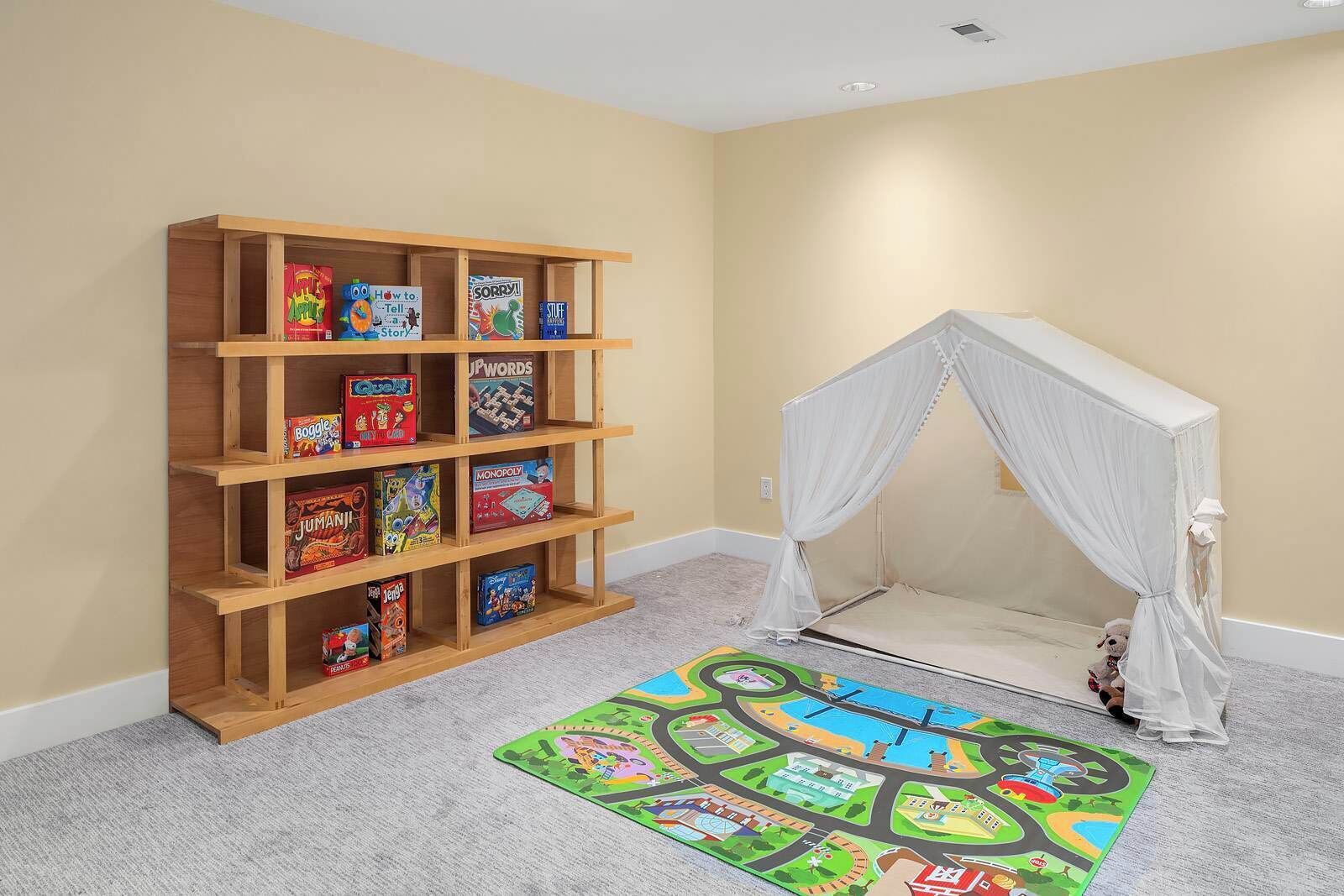 A room with a bookshelf, a play mat, and a canopy bed.