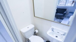 Une petite salle de bain propre, équipée de toilettes, d’un lavabo et d’un miroir.