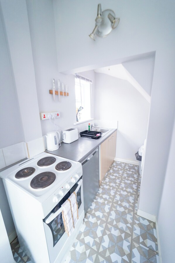 A compact kitchen with a stove, toaster, sink, and patterned floor tiles. - Solo Stay Contractor Pad Near New St Station (Birmingham)
