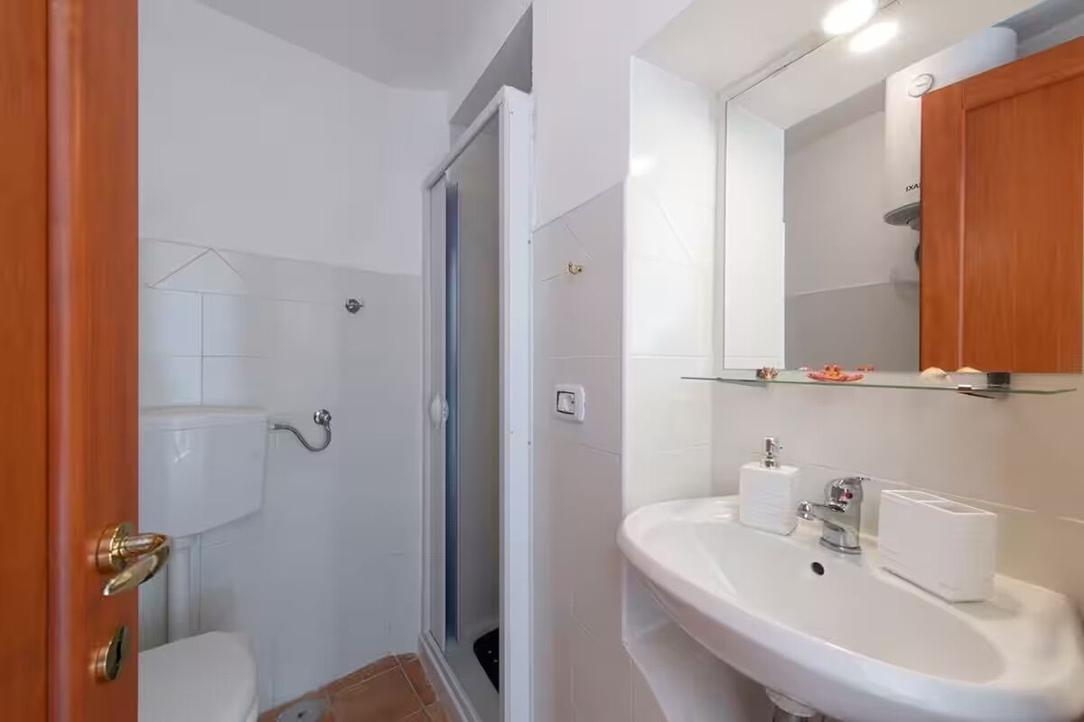 A bathroom with a toilet, shower, sink, and mirror.