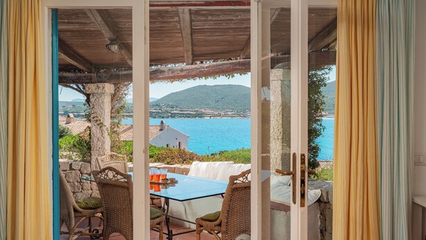 An open patio with wicker furniture and a glass table, overlooking a coastal view with a mountain in the distance. - Casa Turchese by Wonderful Italy (Olbia)