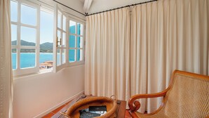 A room with a view of the sea, a wicker chair, a wooden table, and a window with curtains. - Casa Turchese by Wonderful Italy (Olbia)