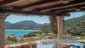 A terrace with a table and chairs overlooking a coastal landscape with mountains and a beach. - Casa Turchese by Wonderful Italy (Olbia)